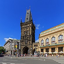 Variété architecturale : Komerční banka, Tour poudrière et Maison municipale. Une vue de la ville : à gauche, un bâtiment gris moderne ; au centre, une tour gothique, noire ; à droite, un bâtiment art nouveau, de couleur claire.