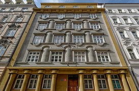 Façade sur rue bicolore, or au premier et dernier niveau, ainsi que sur le pourtour de la façade, gris en son centre (quatre étages), possédant des formes cylindriques (piliers décoratifs notamment).